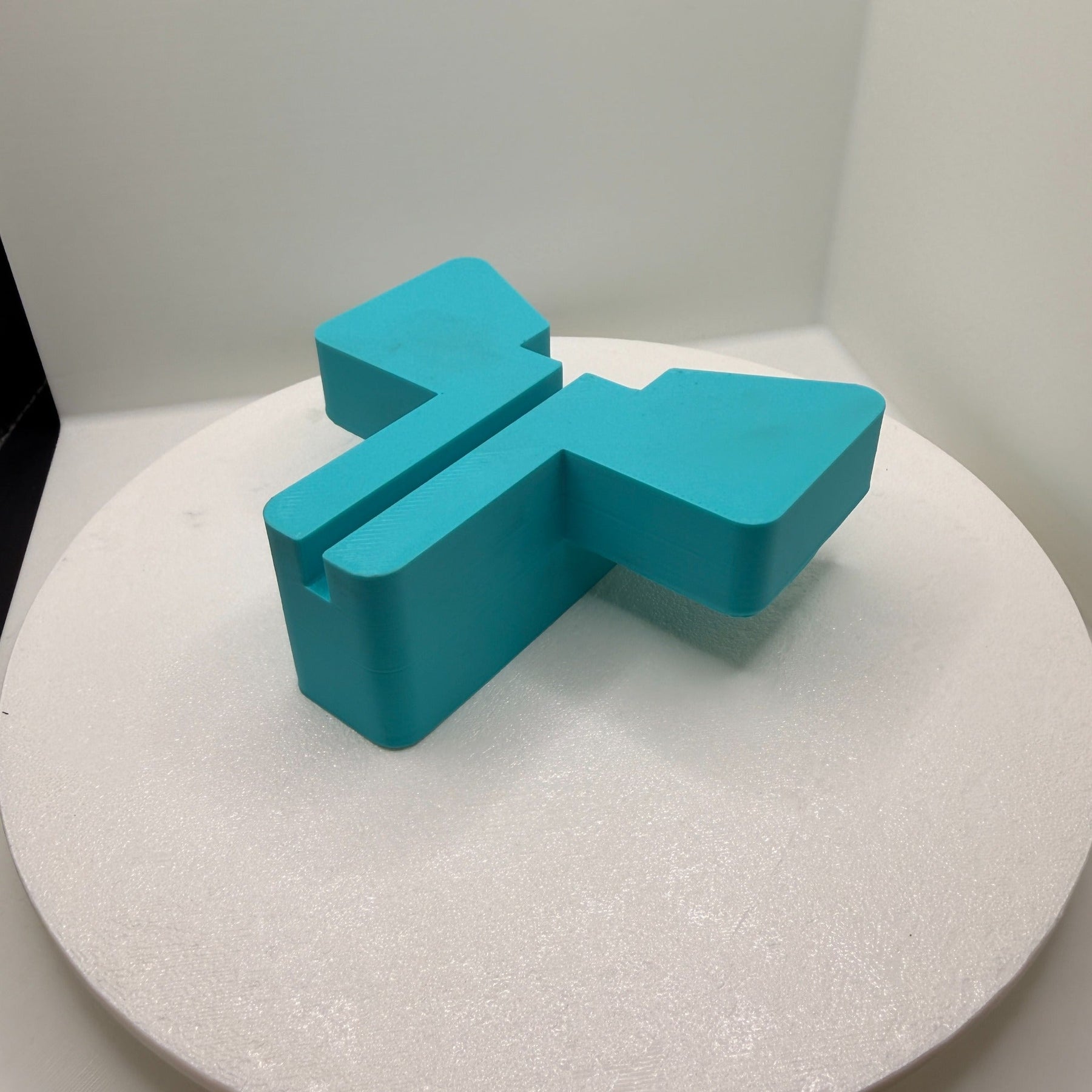 Turquoise two-part 3D-printed CNC jig with shaped supports and a central locating slot