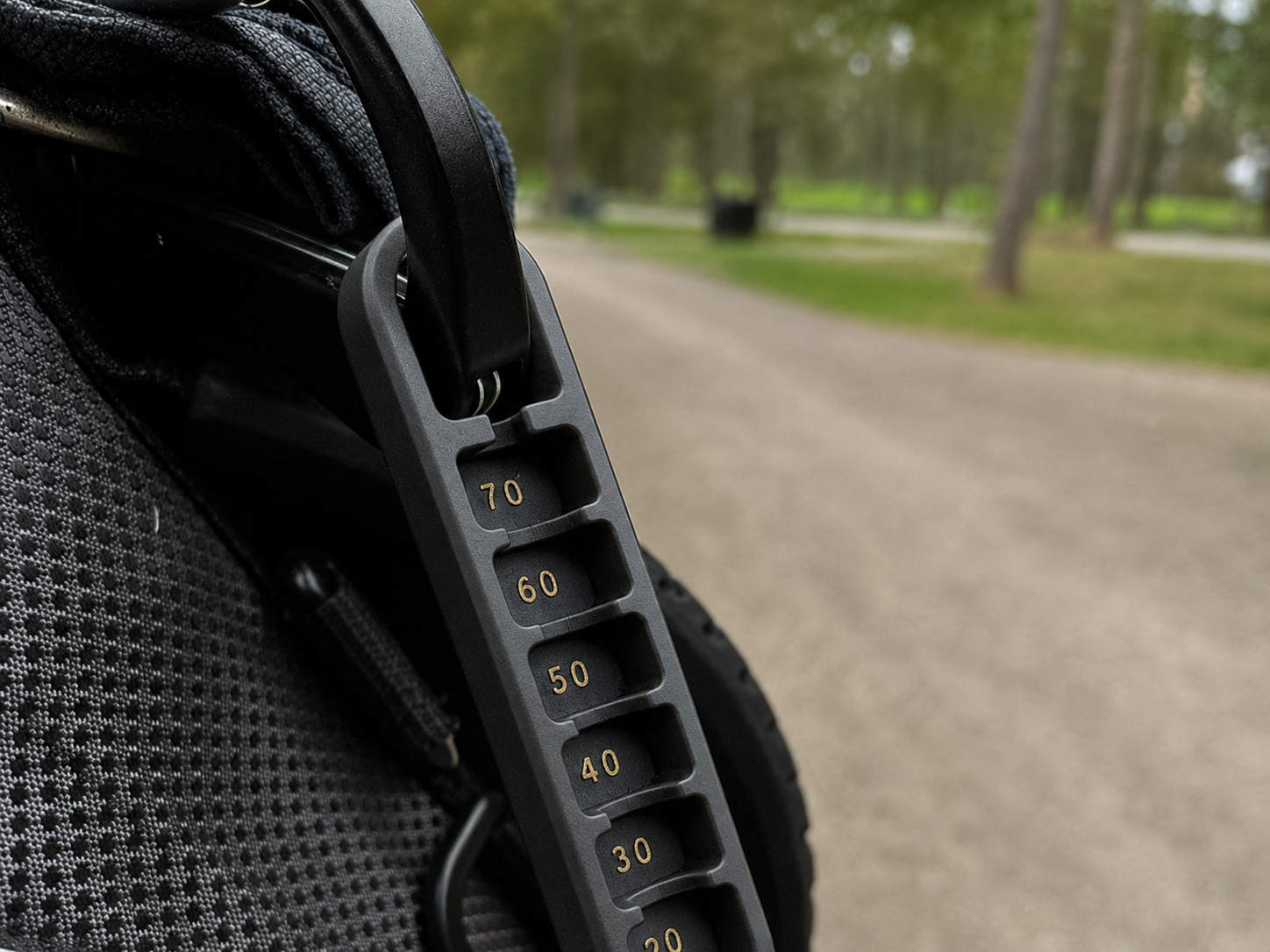 Black Golf Tee Elevator with bronze markings clipped to a golf bag