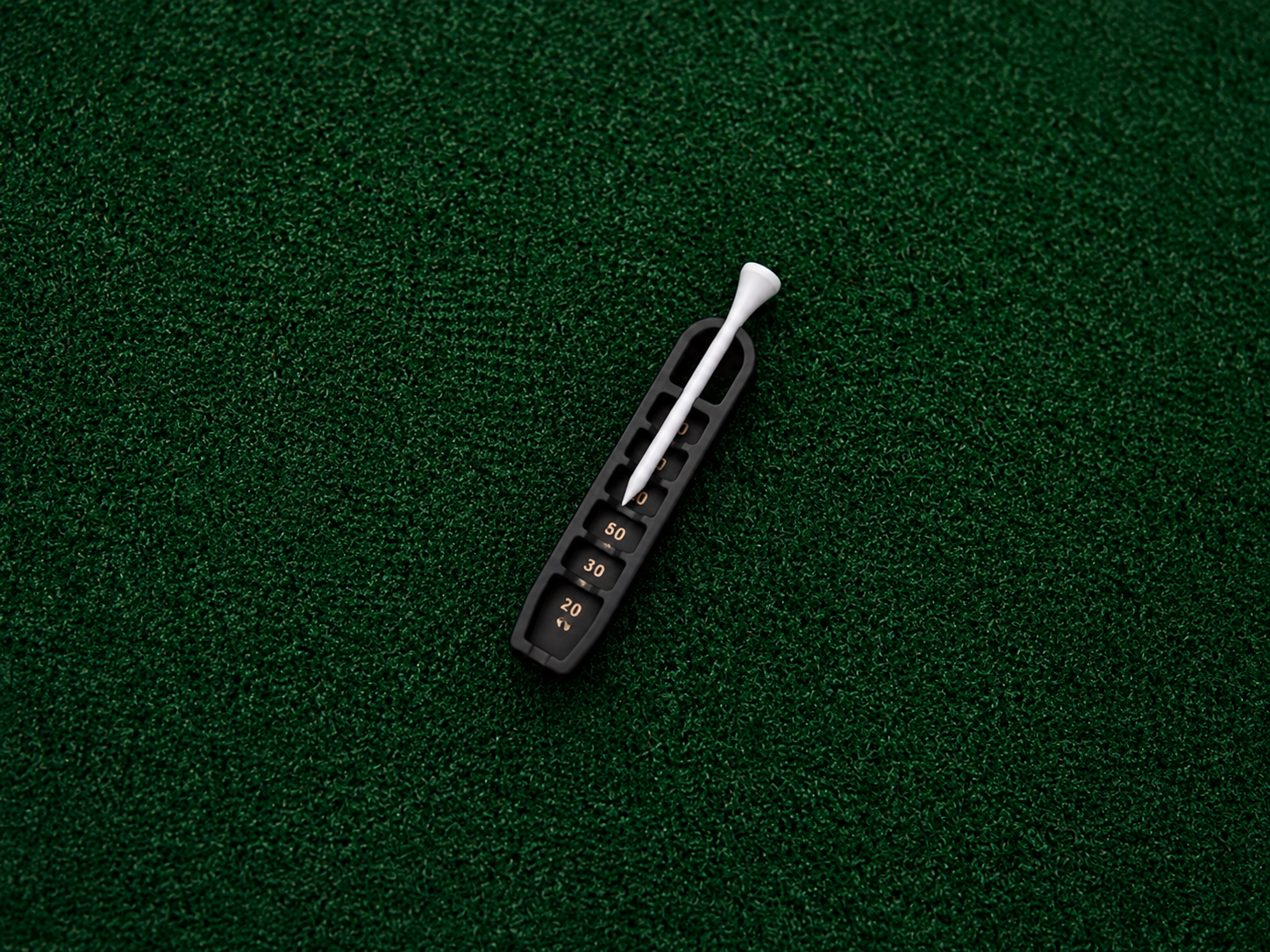 Black Golf Tee Elevator with bronze markings and white tee on putting turf