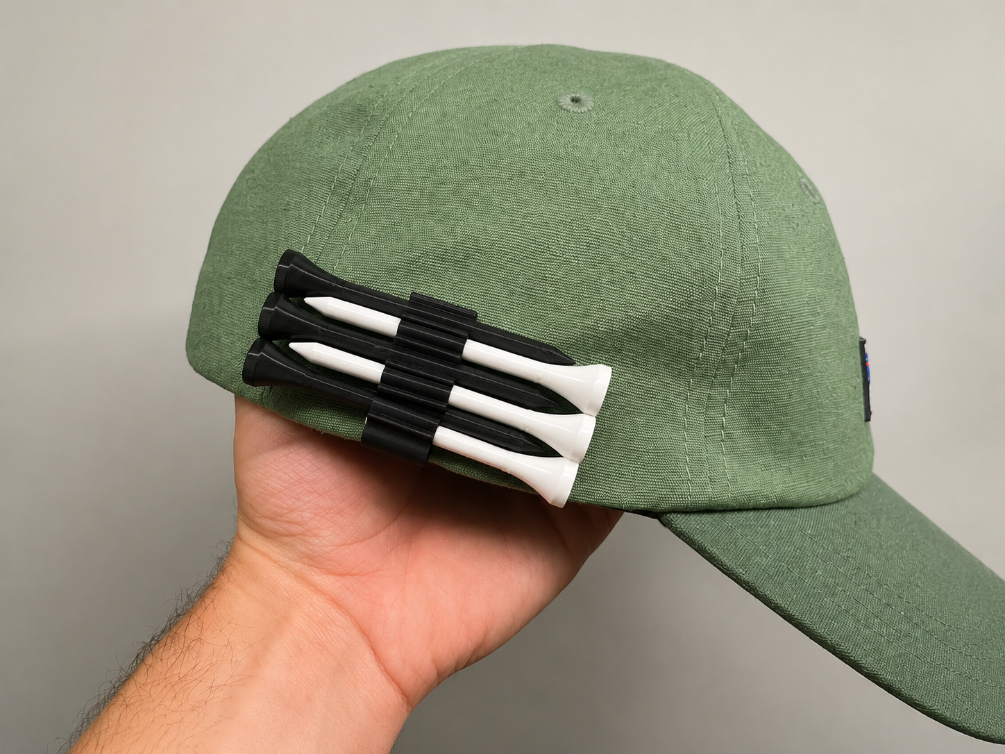 Black Golf Tee Hat Clip attached to a green golf cap