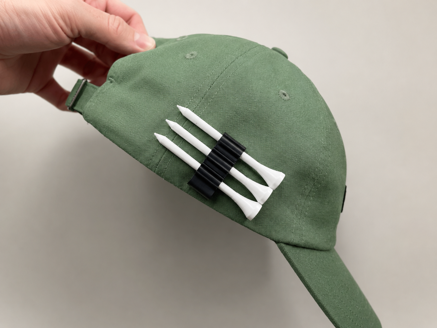 Black five tee holder clipped to a green golf cap