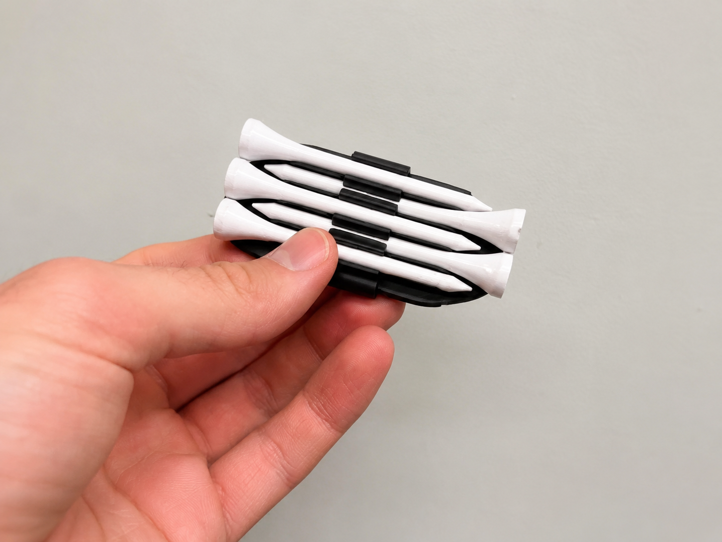 Black Golf Tee Hat Clip held in hand with five golf tees
